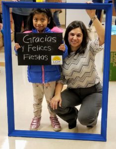 Young girl stands with a frame that says "Gracias y Felices Fiestas" with her new coat. CEO of LCH stands beside the little girl and smiles.